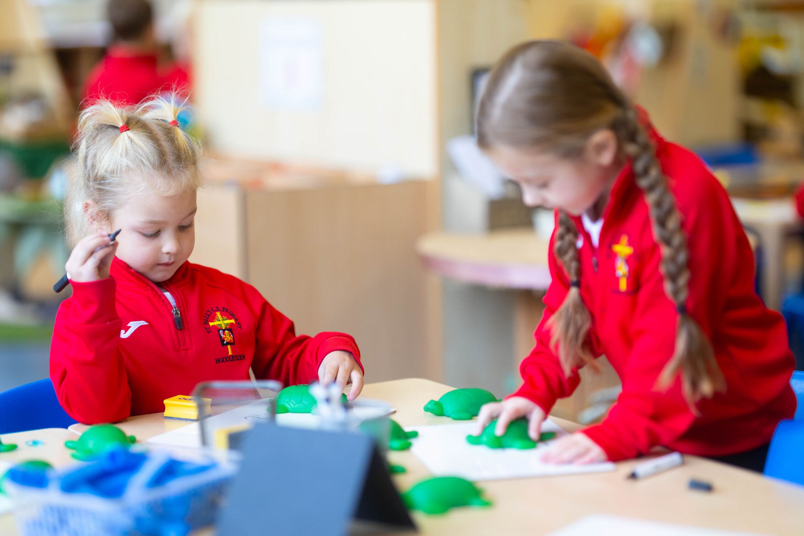 Two pupils in red school uniforms play with green modelling dough at a classroom table